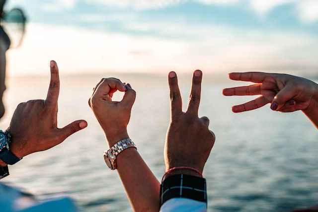 Four hands spelling out the letters L O V E in front of a water background