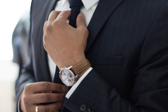 Torso of man in pinstripe suit adjusting his tie, showing an expensive watch on his wrist