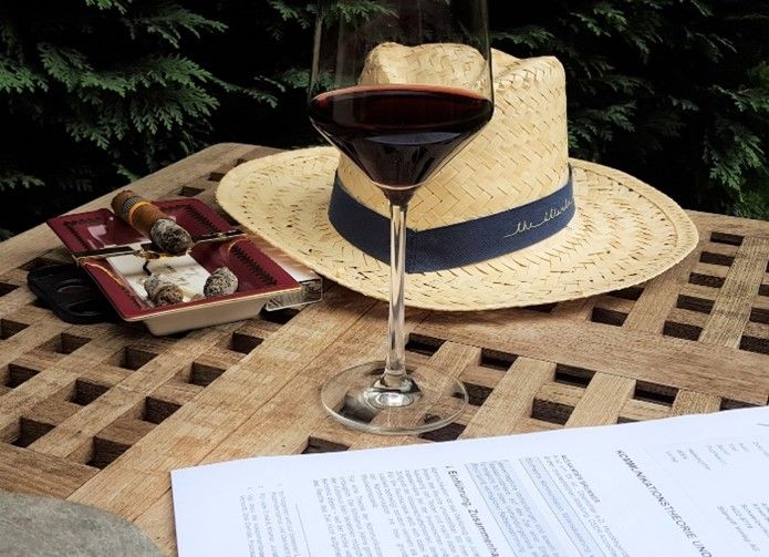 Patio table with straw hat, glass of red wine, and a cigar