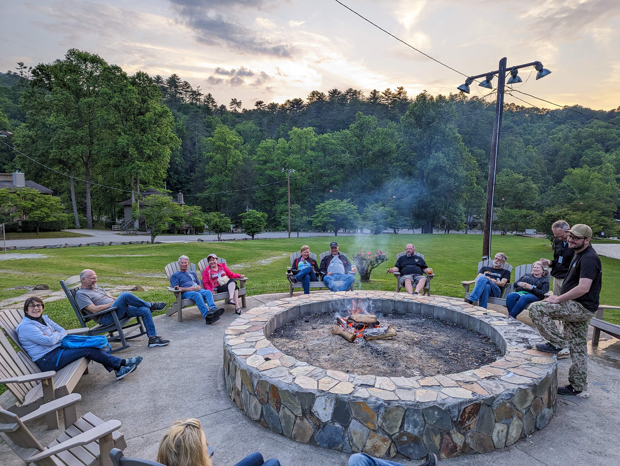 A group of riders sitting around a fire pit with trees in background