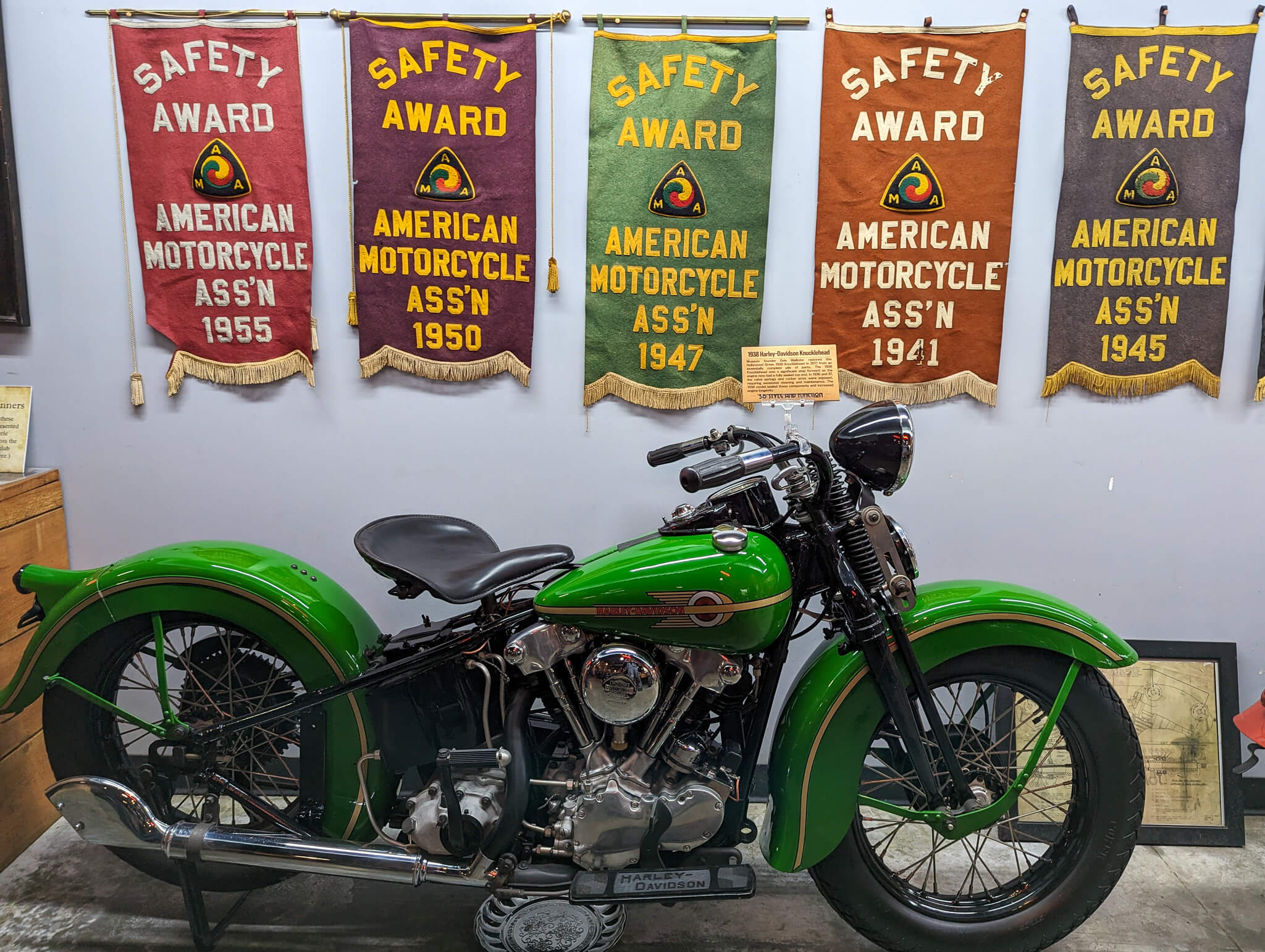 Vibrant green antique Harley motorcycle in front of vintage AMA Safety Awards