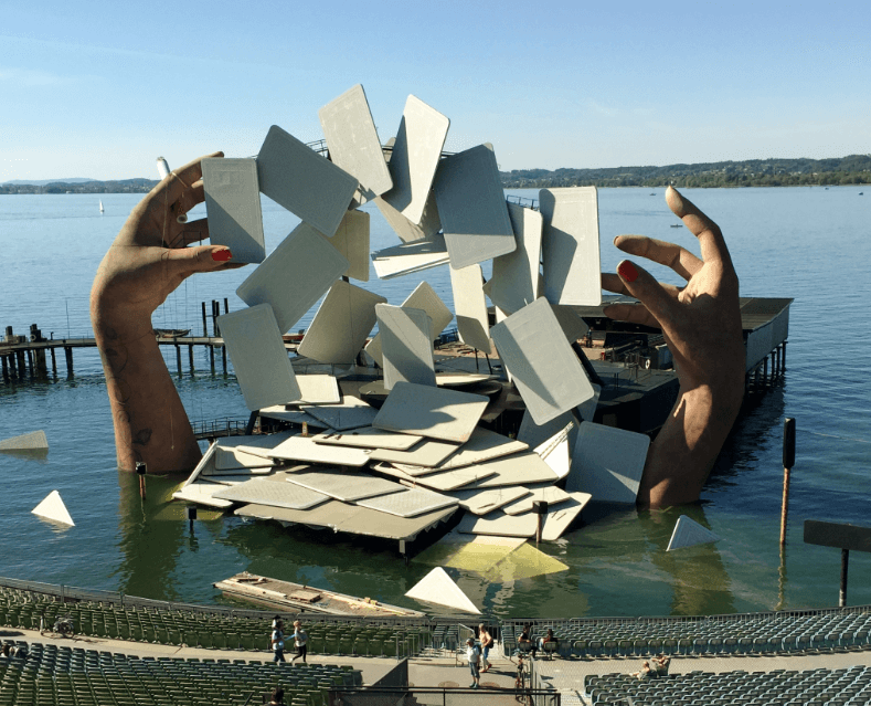 Stage on a lake show giant hands emerging from the water and a huge deck of cards