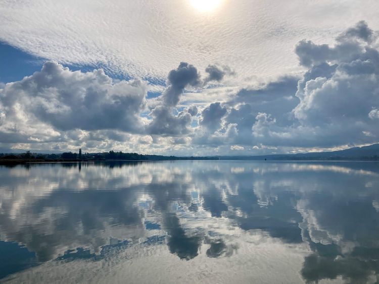 Broad lake view showing reflection of clouds, sky, and sun