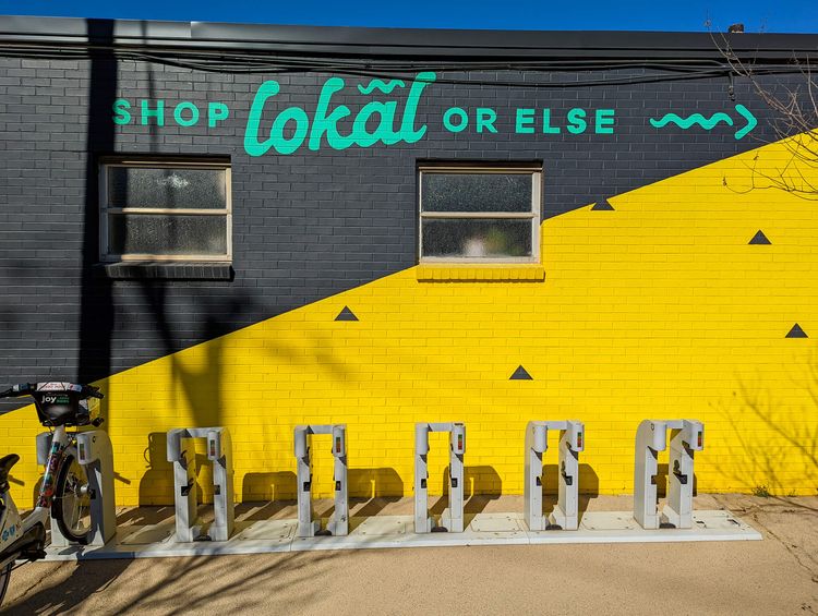 Brick wall painted black on top of 45-degree diagonal and yellow on bottom. Painted words "shop lokal or else"