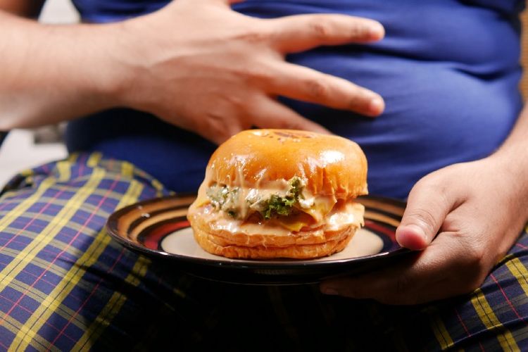 Man holding cheesy burger in front of large stomach
