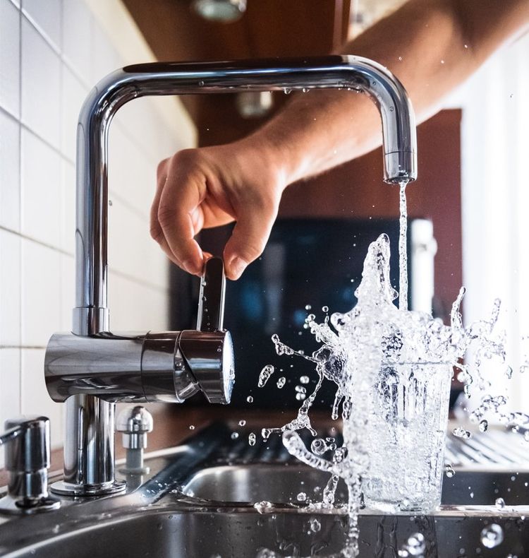 Water pouring briskly from silver faucet into overflowing glass