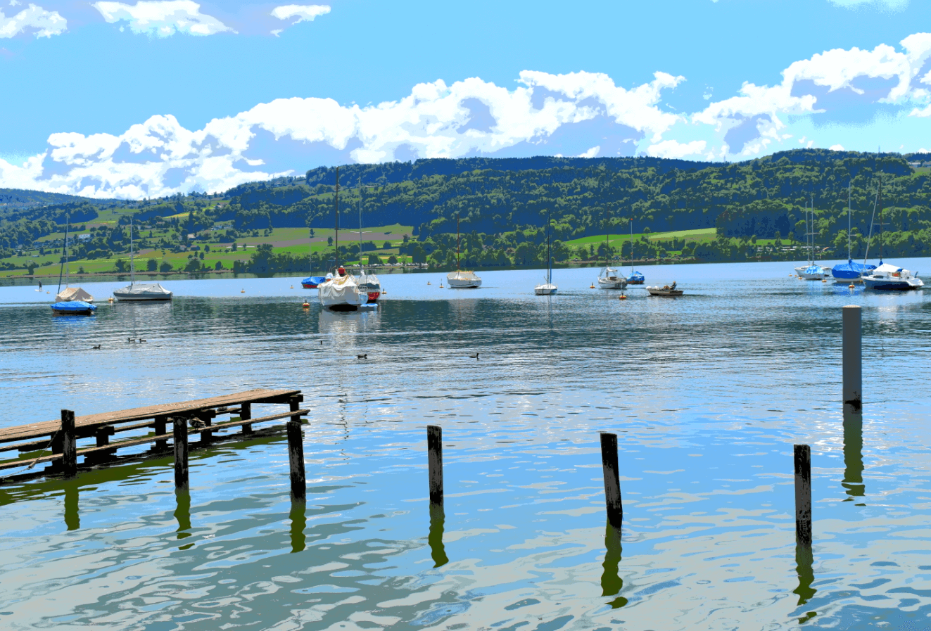 Lake with sailboats, small pier in foreground, green hills in background