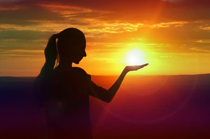 Woman in silhouette with sun in the palm of her hand