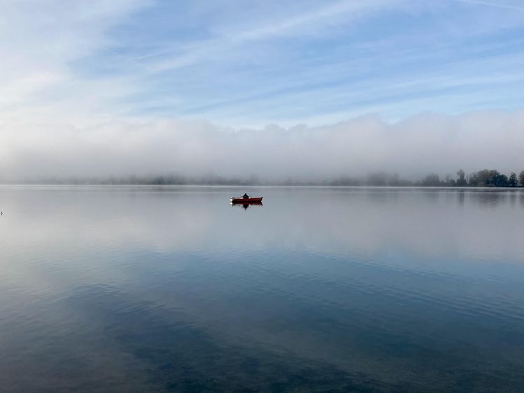 A small rowboat with a solitary fisherman on a large, smooth lake surface