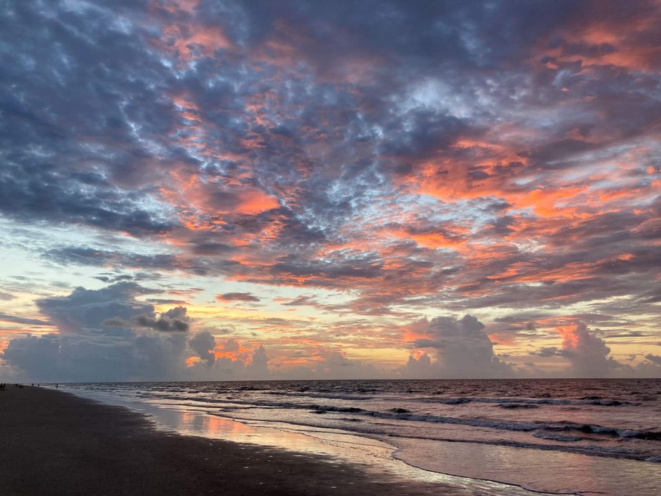 Orange and pink colored clouds in a big sky over an ocean seen from the beach