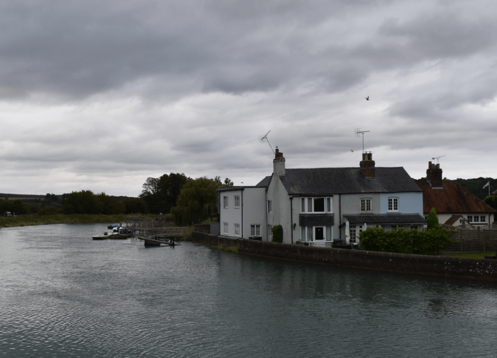 Stone house bordering a wide river under a gray, clouded sky - Moral Letters to Lucilius