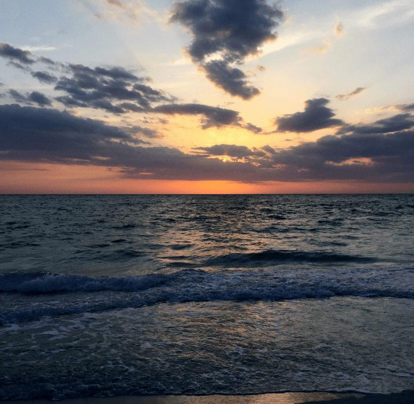 Orange sunset behind gray clouds over a placid ocean