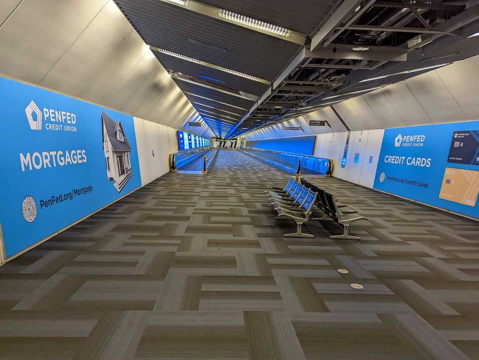 Empty airport walkway, with seats in foreground and escalators stretching off in distance