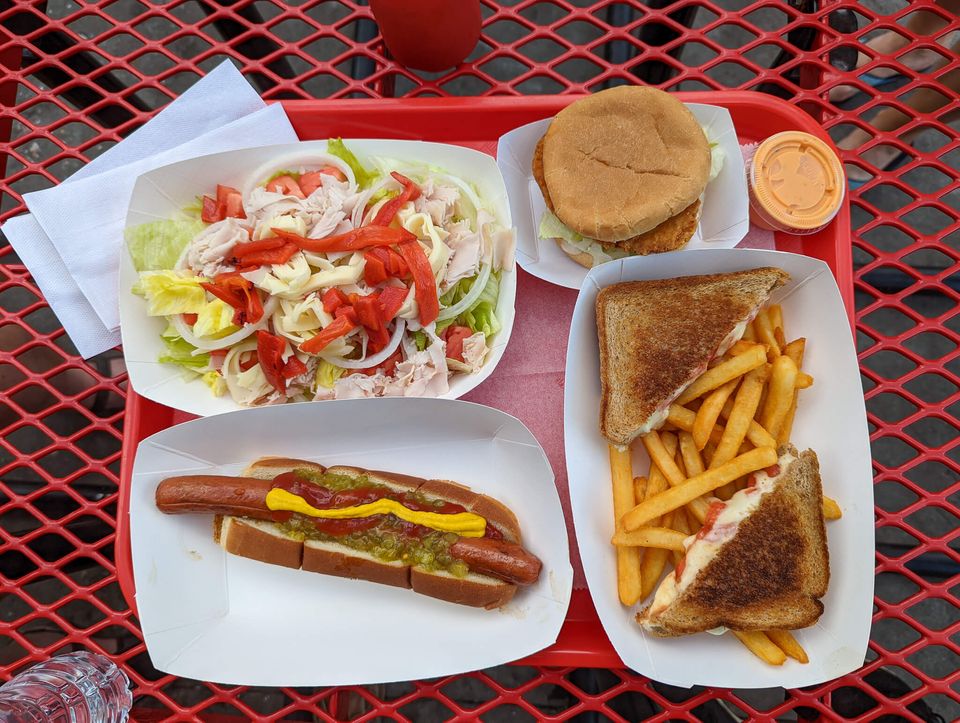 Plastic tray with hot dog, salad, chicken sandwich, and grilled cheese with fries