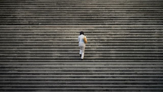 A woman in white seen from behind climbing a long set of stairs