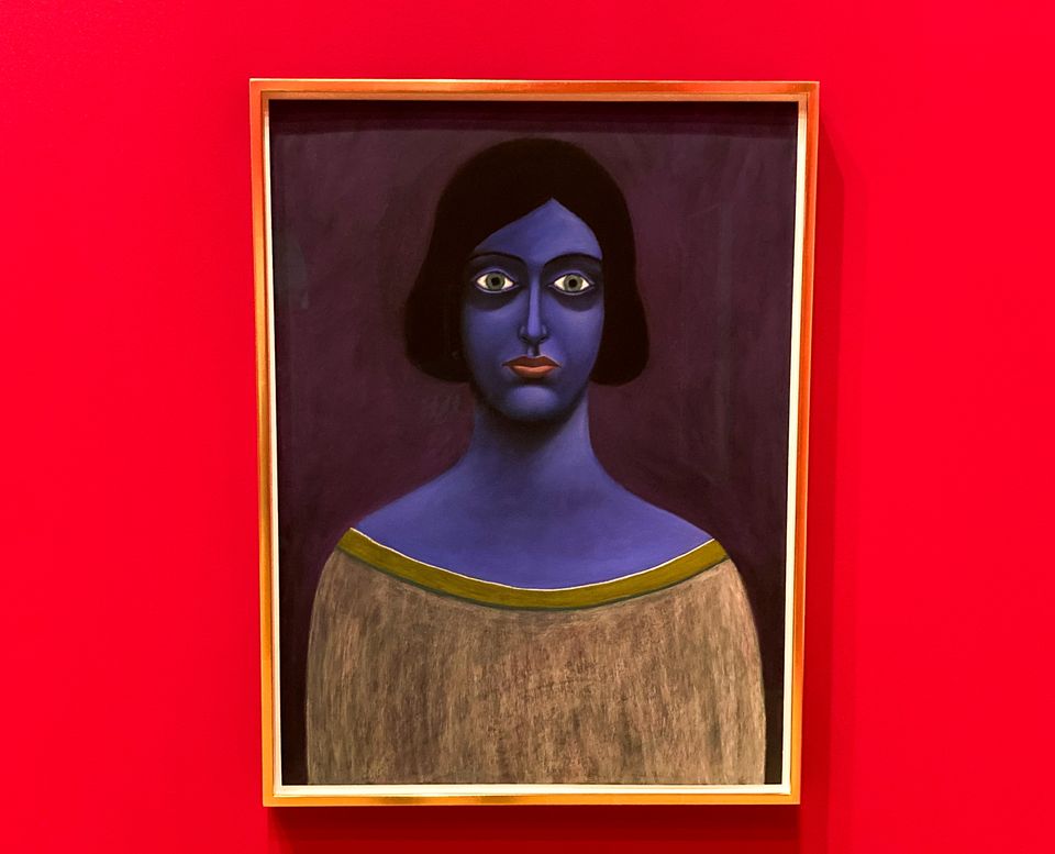 Painting of blue-skinned woman with black hair. Bright red wall behind painting