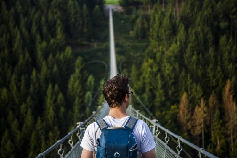 Man at one end of long narrow suspension bridge