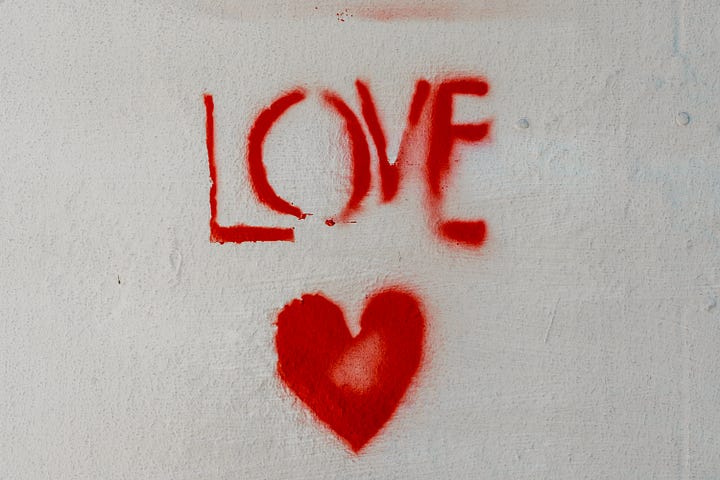 Word LOVE painted in red on a white wall with red heart underneath
