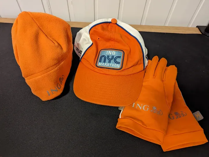 Bright orange winter hat, gloves, and baseball cap from the NYC Marathon